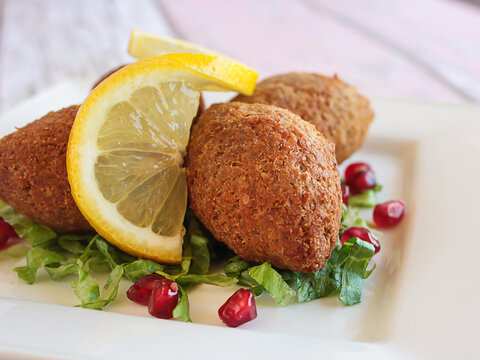 KEBBAH, kibbeh, kibbe or kubbeh with lemon slice and pomegranate seeds closeup served in dish isolated on table side view of arabic fastfood