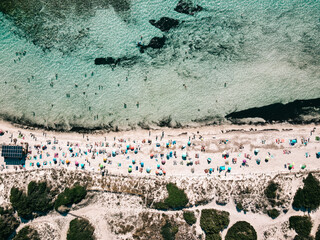 Aerial view of sandy beach with colorful umbrellas, unrecognizable people, sea coast with transparent blue water at sunny day in summer. Travel in Mallorca, Balearic islands, Spain. Top view. Tropical