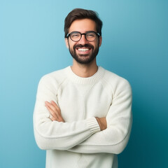 Young handsome man with beard wearing casual sweater and glasses over blue background happy face smiling with crossed arms looking at the camera. Positive person.