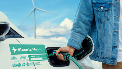 Hand insert EV charger and recharge electric car from charging station displaying futuristic...