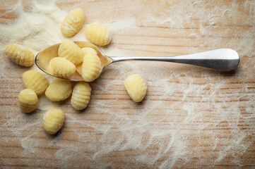 Potato gnocchi with durum wheat flour in silver spoon on pastry board, top view, space for text, close-up.