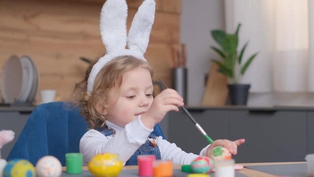 Happy child sharing joy while painting Easter eggs with plant and tableware.