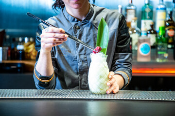 barman prepara un cocktail de piña colada con hoja de piña en un vaso decorado sobre la barra de...