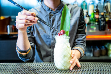 barman prepara un cocktail de piña colada con hoja de piña en un vaso decorado sobre la barra de...