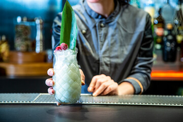 barman prepara un cocktail de piña colada con hoja de piña en un vaso decorado sobre la barra de un cocktail bar exclusivo por la noche en ambiente de fiesta, camarera close up