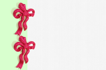 Border made with pink glittered bows, Christmas ornament and white paper with texture. Creative minimal art. Flat lay. Minimal composition. Creative concept with copy space. Border arrangement.