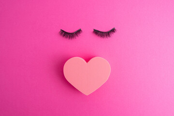 False eyelashes, makeup sponge in the shape of a heart for eye makeup on a colored background....