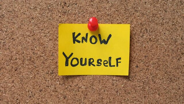 A yellow paper note with the phrase Know Yourself on it pinned to a cork board. Close up.