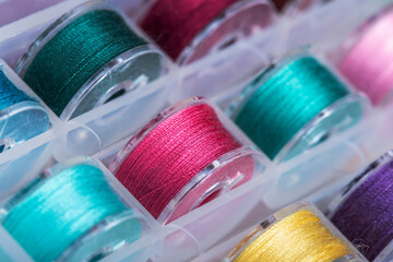 Plastic bobbins for a sewing machine with brightly colored threads in a storage box.