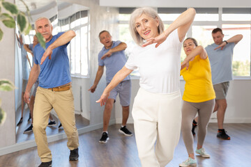 Positive elderly woman practicing Tai Chi with group of aged people, promoting health and wellness...