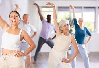 Young girl coach oversees mentoring group of elderly clients in fitness studio. Multiracial group...