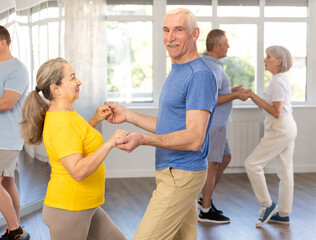 Cheerful senior man practicing passionate samba with interested woman in dance class for adults....