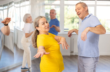 Smiling senior woman dancing vintage twist, popular in sixties, with characteristic arm movements paired with man in modern dance studio. Nostalgia for youth. Active hobbies concept.. - obrazy, fototapety, plakaty