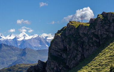 hiking in Austria - a mountain peak with a cross on a background of snowy alpine peaks - Powered by Adobe