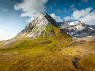 Fototapeta premium drone shot of majestic mountains in the heights in the middle of a sunny day surrounded by clouds, wild nature in svalbard, useful for magazines and magazines, traveling for mountains, svalbard