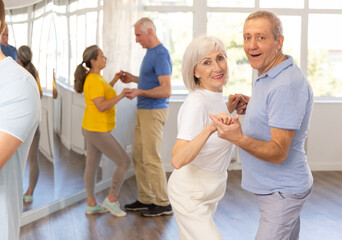 Cheerful senior woman practicing passionate samba with interested attentive man in dance class for...