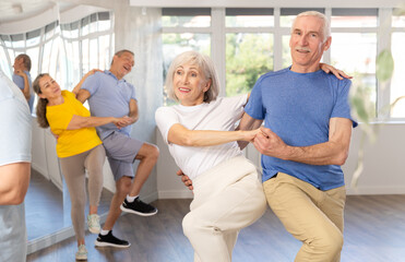 Obraz premium Enthusiastic senior couple, woman and man in sportswear, participating in group class for aged people, practicing energetic upbeat jive. Social dancing concept..