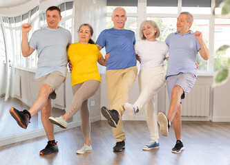 Group of elderly men and women dancing traditional folk dance in row in studio