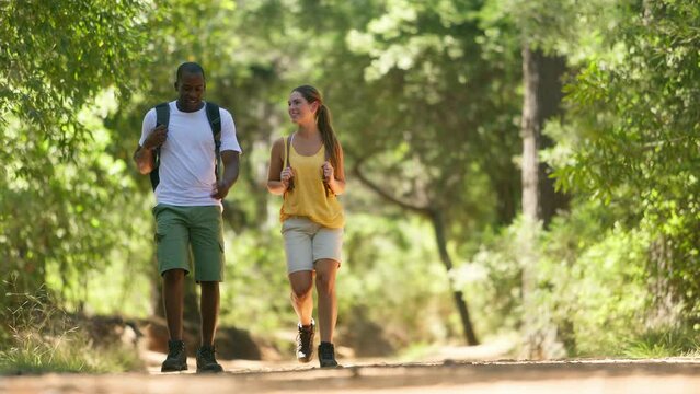 Young active couple wearing backpacks hiking along trail through summer countryside - shot in slow motion