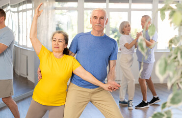 Fototapeta na wymiar Happy smiling elderly woman enjoying impassioned merengue with male partner in latin dance class. Social dancing concept..