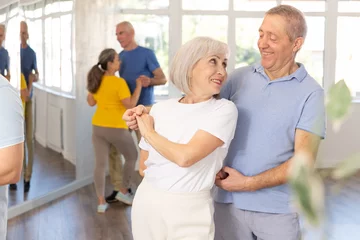 Photo sur Plexiglas Anti-reflet École de danse Happy smiling elderly woman enjoying impassioned merengue with male partner in latin dance class. Social dancing concept..