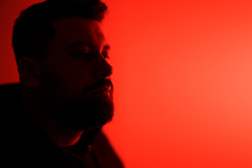 Side profile of a pensive man bathed in a red neon light, evoking a moody atmosphere
