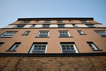 Obraz premium Stone and brick apartment building view from sidewalk looking up against clear blue sky.
