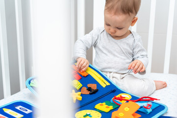 Baby playing with busy book sitting in crib. Concept of smart books and modern toys