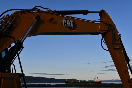 CAT excavator with Columbia River and cargo ship in background, sunset.