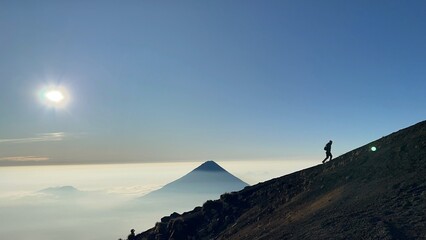 Hiking with a silhouette of a hiker against the backdrop of a volcano towering over the clouds in...
