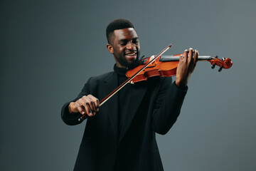 Elegant young african american man in black suit playing violin on grey background at studio