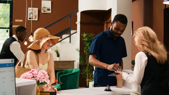 Hotel guests checking in at reception, signing electronic documents on tablet. Travellers at front desk filling in registration papers for room reservation on summer seaside holiday. Handheld shot. - Powered by Adobe