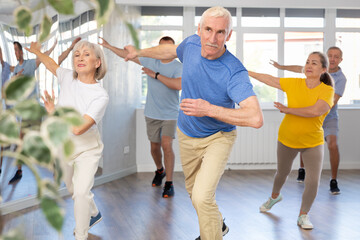 Expressive cheerful gentleman participating in upbeat Zumba class for group of seniors in mirrored fitness studio