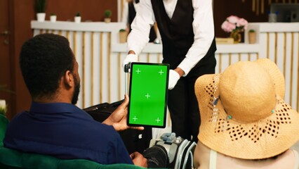 Guests holding tablet with greenscreen in lounge area lobby, using isolated display together in...