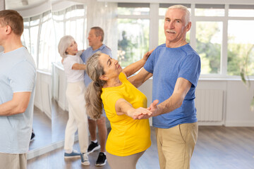 Happy aged woman learning to dance Viennese waltz with partner in dancing class. Active hobby of...