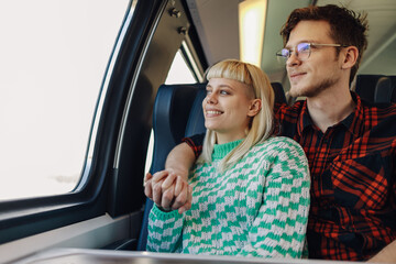 A young couple is traveling with train and looking trough the window.