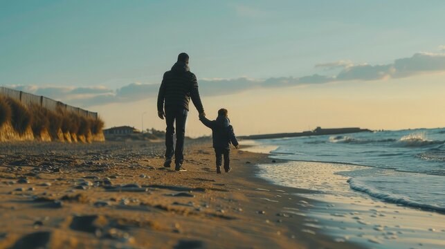 Rear view of father and son holding hands while walking on sand at beach