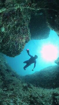 Freediver swims underwater in the sea and explores the rocky bottom