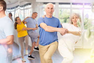 Group of elderly men and woman in sportswear learning to dance latin salsa dance in dance class