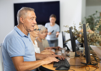 Interested senior man attending computer class, learning basics of digital technology under...