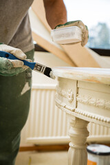 Middle-age man painting old wooden table with paint brush in white color. Furniture restoration, DIY repair, repair by oneself and home improvement. Recycling and sustainable lifestyle