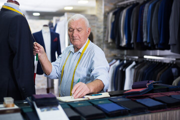Mature tailor makes measurements of a business suit at studio