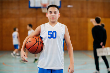 Portrait of a basketball kid posing with a ball on court during training.