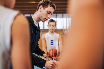 A young basketball coach is working on tactics with his junior team.