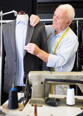 Mature tailor sews a new jacket on a mannequin in a sewing studio