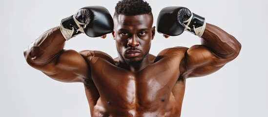 A man with a pair of boxing gloves placed on his head looks strong and determined, standing in a white setting. His posture exudes power and readiness for a match. - obrazy, fototapety, plakaty