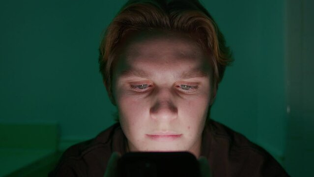 Tight shot of a boy's face lit up by the screen of a smartphone