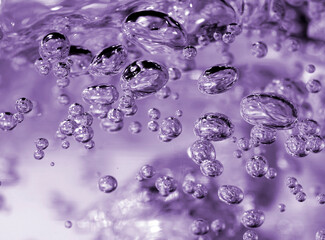 A close-up photograph of effervescent water bubbles in motion, captured with a purple hue creating...