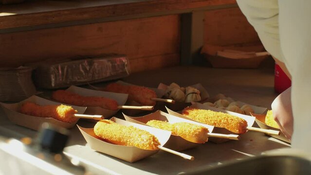 Cooking corn dogs in boiling oil close-up. Traditional asian corndog snacks street food. Fried sausage in breadcrumbs on a stick. Korean Chinese street local market with traditional food. American