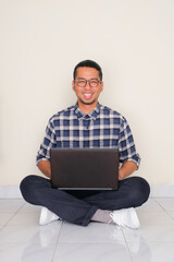 Adult Asian man sitting crossed leg with laptop on his lap showing happy expression